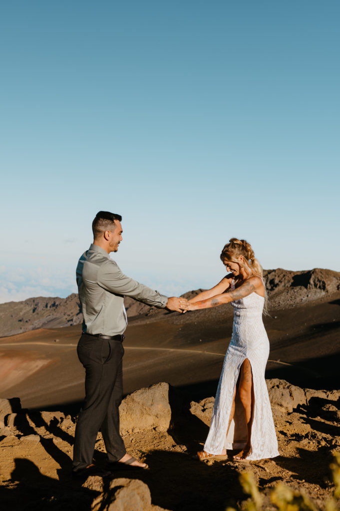 A bride and groom playfully hold hands in Haleakala National Park