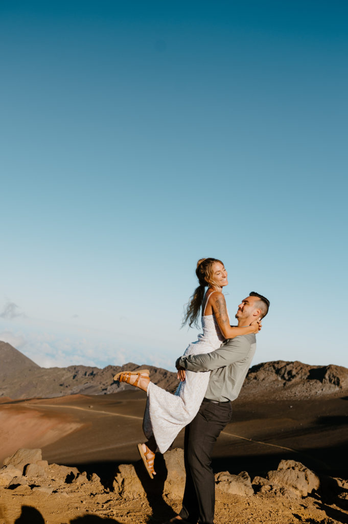 A groom lifts up his bride at Sunset atop Haleakala Summit