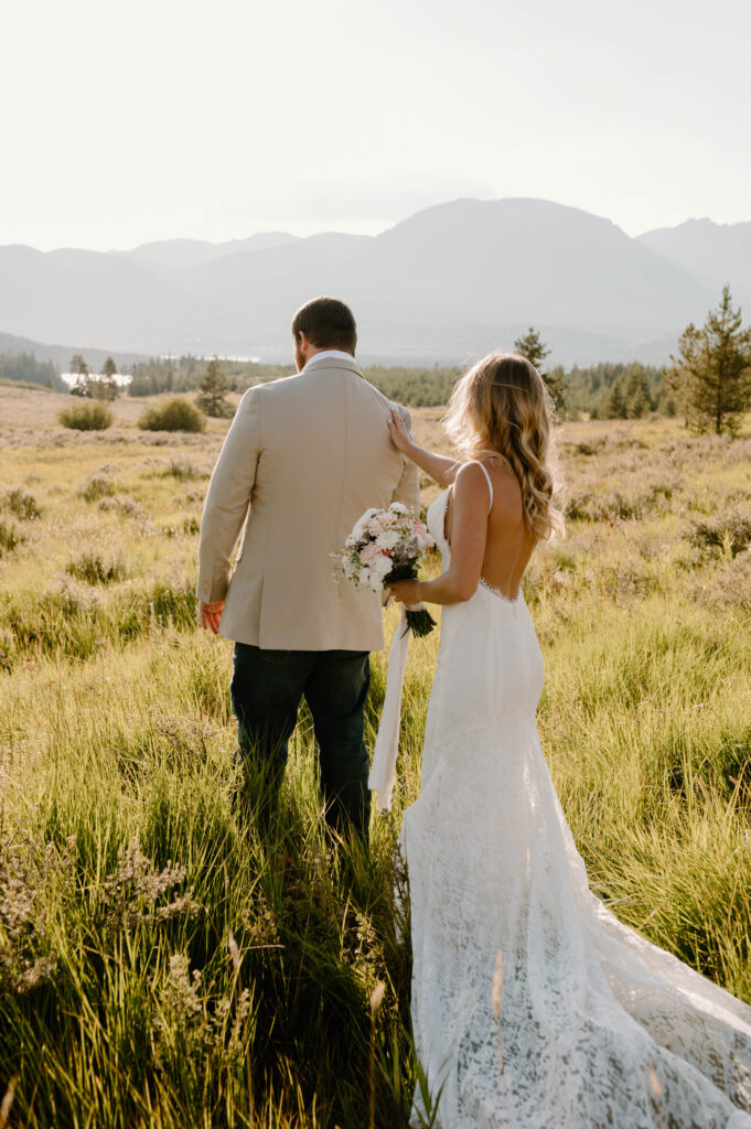 A woman touches her groom's shoulder before their first look. 