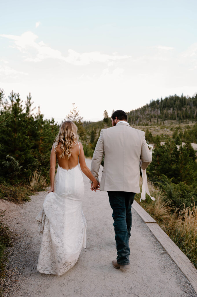 A newly married couple walks hand and hand to their getaway car after their elopement in the Rocky Mountains. 