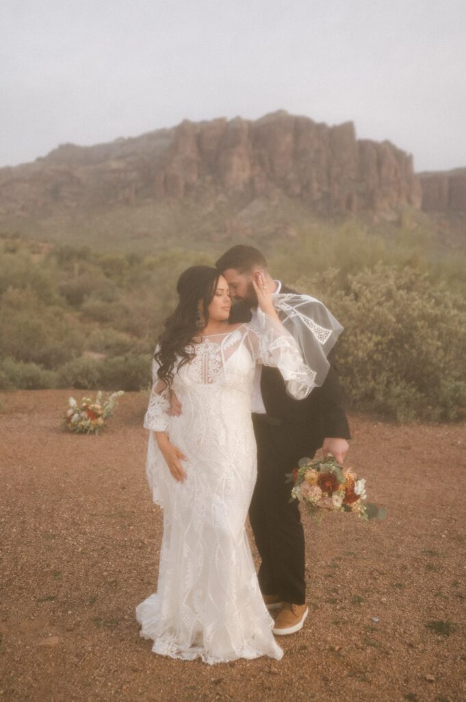 A couple poses in front of a rock formation with wedding florals before their elopement