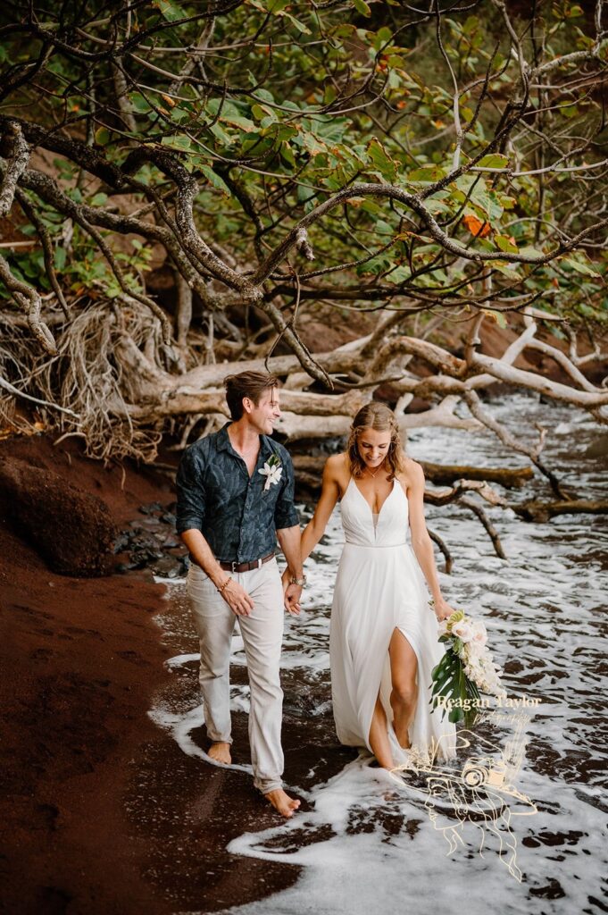A couple walks along a sandy beach with wedding florals