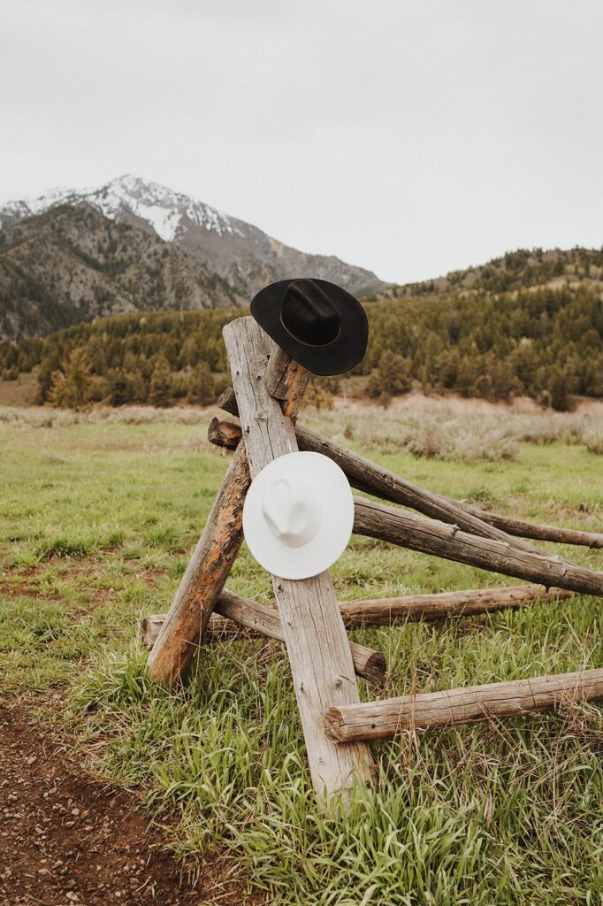 One white and one black cowboy hat hang on a fence in a pasture  