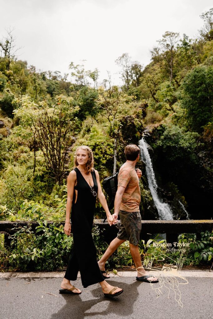 A couple walks past a waterfall on a road near Red Sand Beach