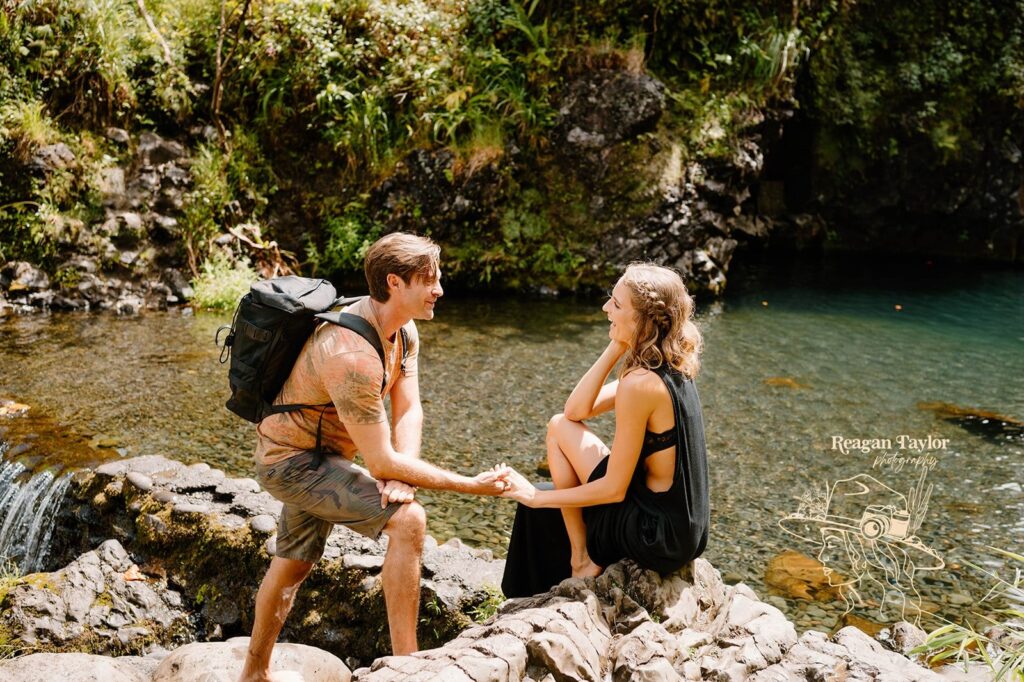 A couple on a backpacking trip to a waterfall pose at the edge of the water on a rock