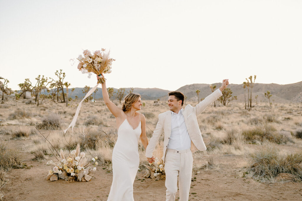 A couple raises their hands in celebration of their wedding in Joshua Tree