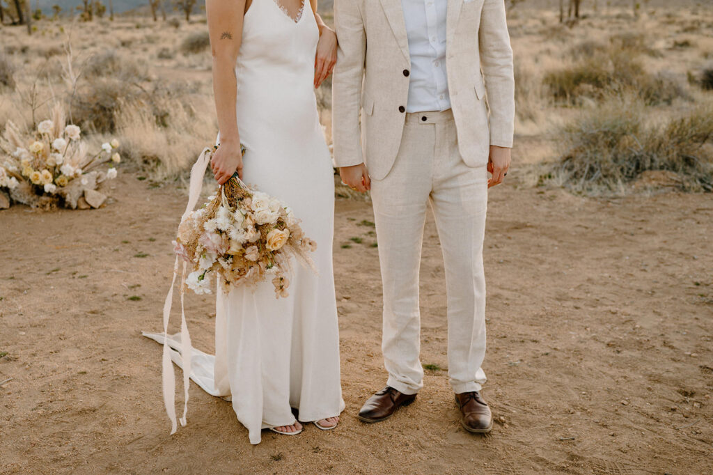 Newlyweds pose to showcase their neutral wedding attire and florals