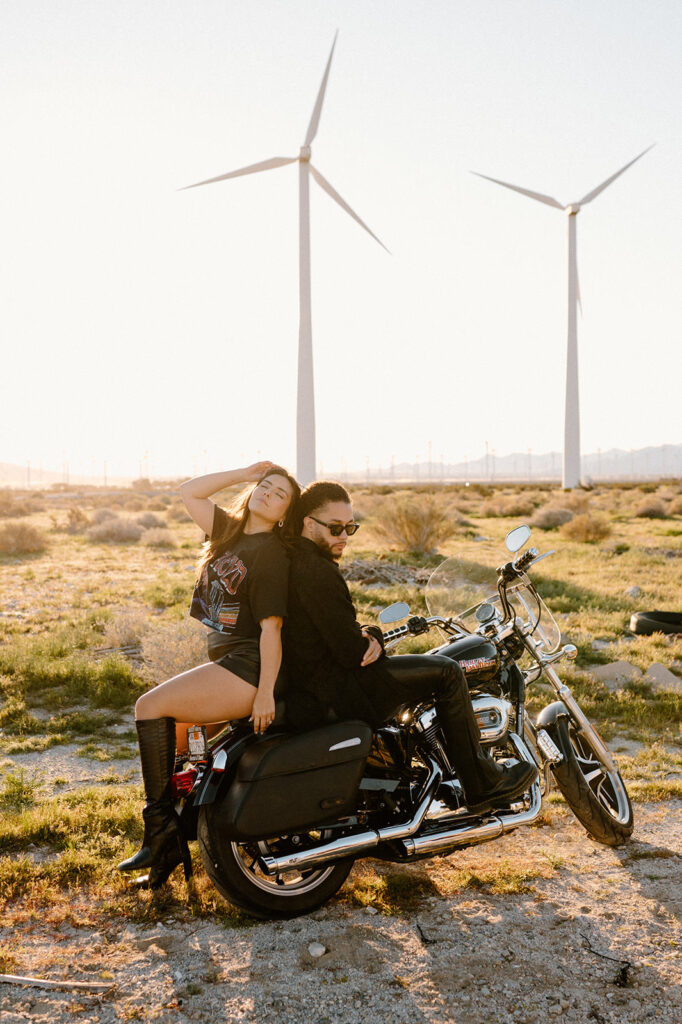 A woman poses on the back of a motorcycle while her husband leans against her