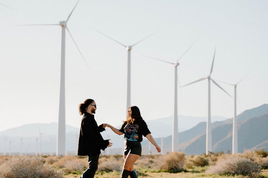 A couple poses playfully in front of windmill field near Palm Springs