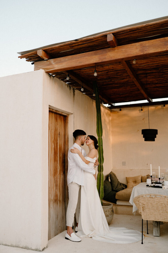 A newlywed couple poses beneath a wooden overhang at a elopement location in Tulum