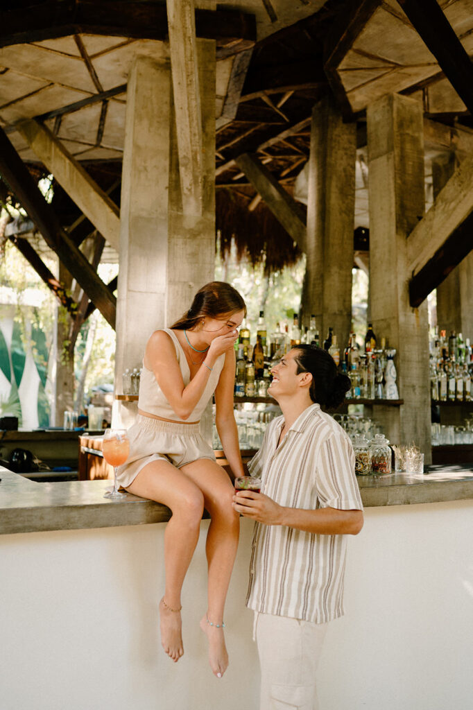 A woman laughs with a man during their engagement at an outdoor jungle bar in Tulum