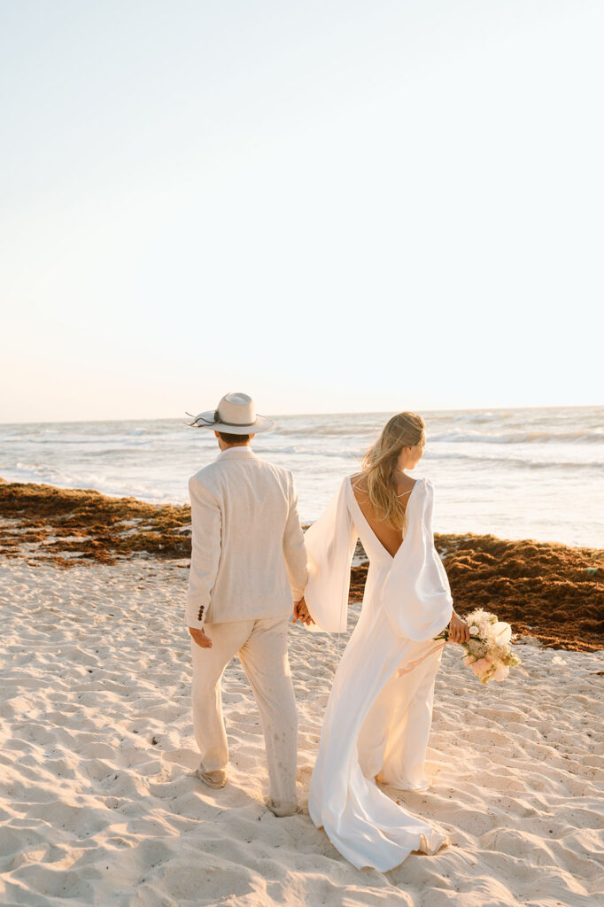 A couple walks along a beach in Mexico at Sunset before their Tulum elopement ceremony