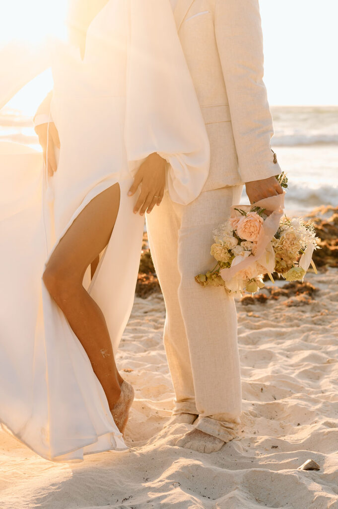 A couple holds on another close and is seen from the waist down with wedding florals.