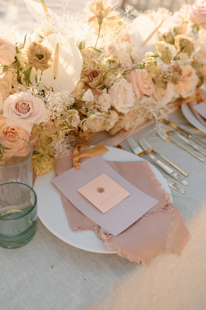 A plate setting for a wedding is seen with a pink napkin and place cards.