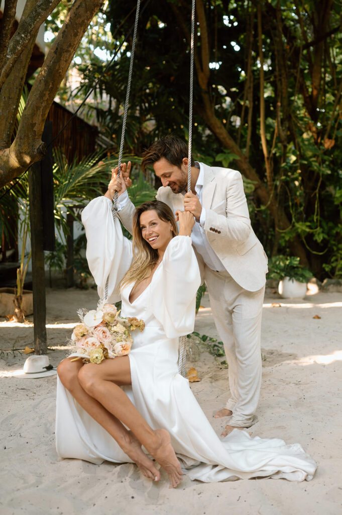 A woman sits on a jungle swing near her husband during their Tulum elopement