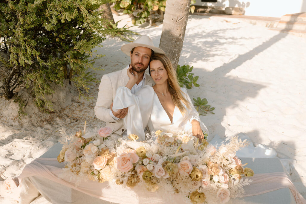 A couple poses with dried wedding florals in the sand for their Casa Violeta wedding