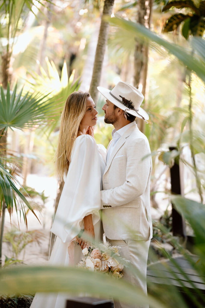 A couple stands near palms during their destination wedding in Mexico