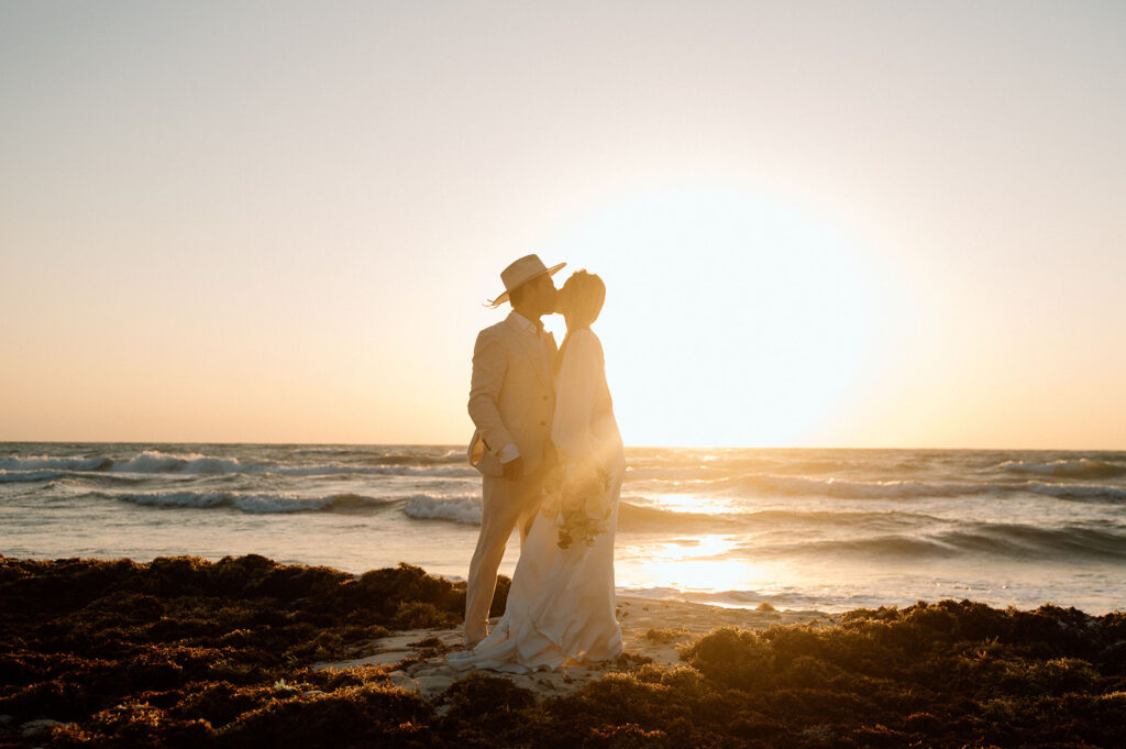 A couple kisses on a beach in Mexico during their elopement ceremony.
