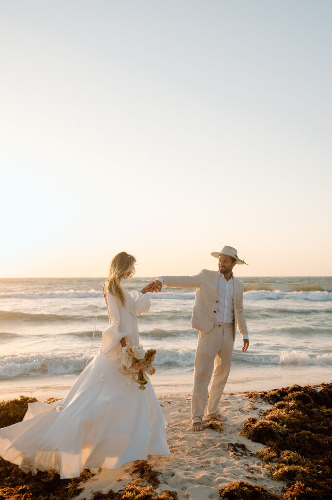 A couple stands apart from once another while holding hands at Sunset near Casa Violeta during their elopement
