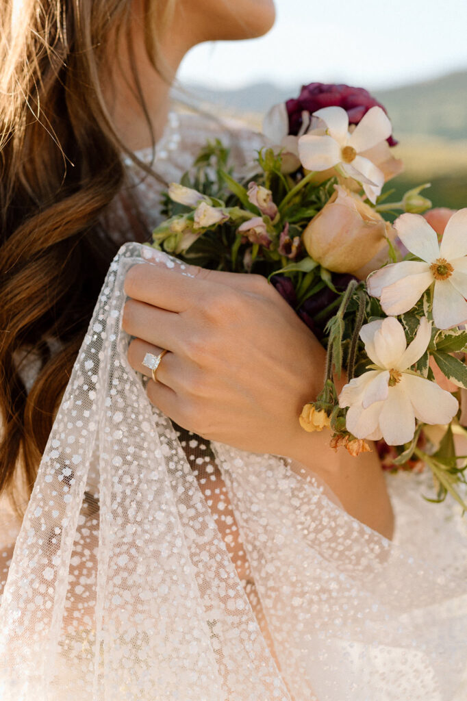 A bride holds here veil while showing off here wedding ring and elopement florals.