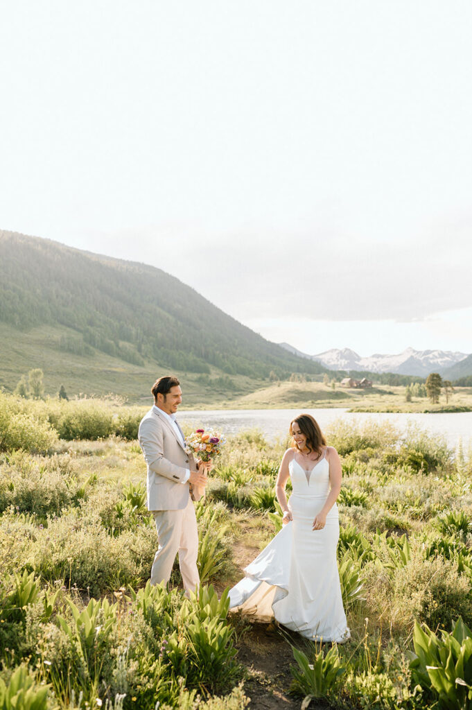 A groom holds wedding florals while admiring his bride in Crested Butte.