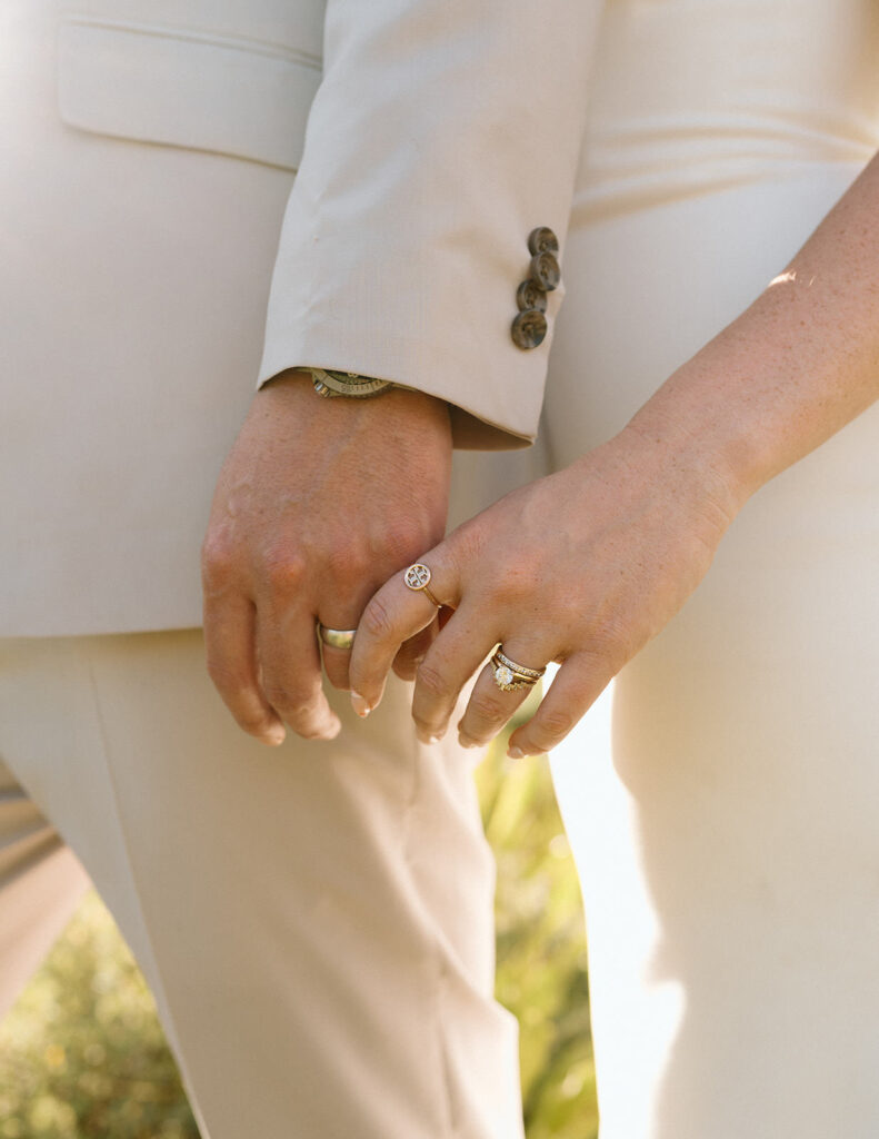 A couples wedding rings are show while they hold hands.