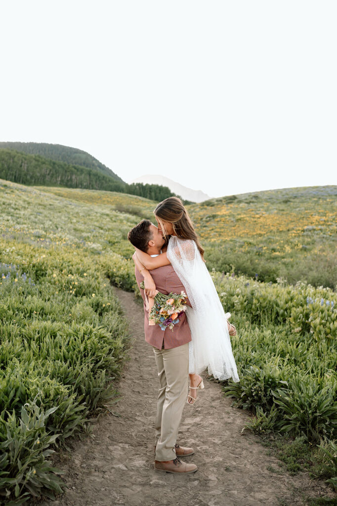 A couple kisses along a hiking path in an alpine valley.