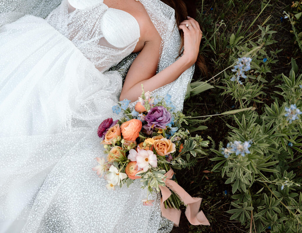 A bride lies in a meadow near wedding florals.