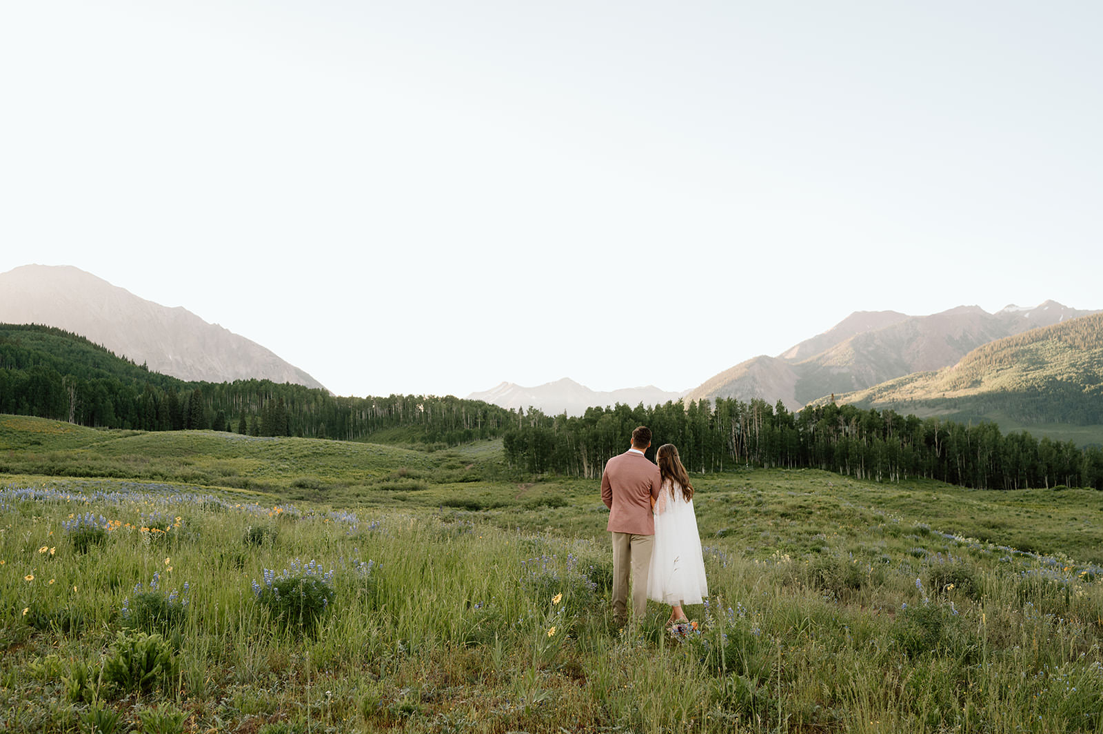 A man and women walk through a meadow of wildflowers in Crested Butte after their elopement.