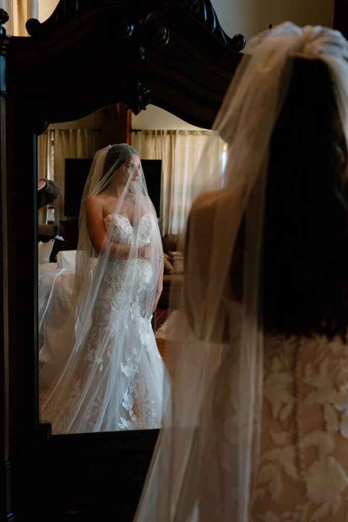 A bride is seen wearing a white wedding gown in the reflection of aa mirror at Golden Mountain Ranch.