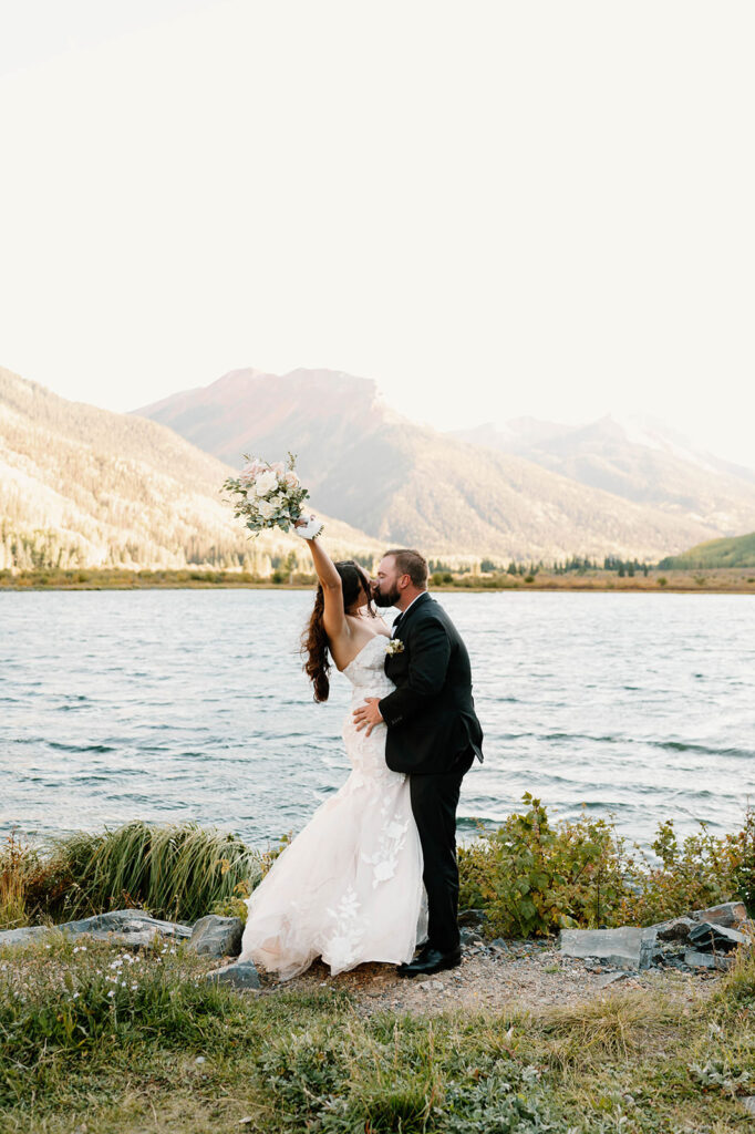 A bride and groom kiss on the shores of an alpine lake in Ouray, Colorado. 