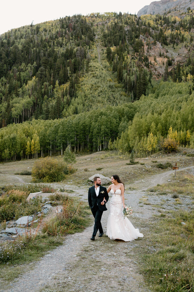 A couple walks along a hiking trail in wedding attire during their mountain elopement.