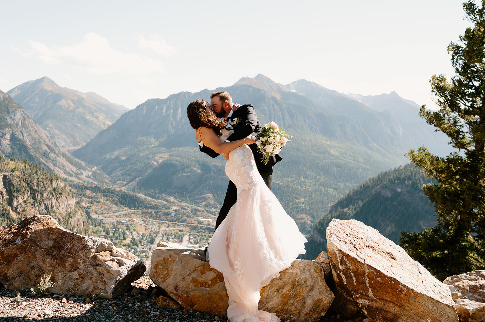 A newlywed couple shares a kiss atop a mountain overlooking Ouray.