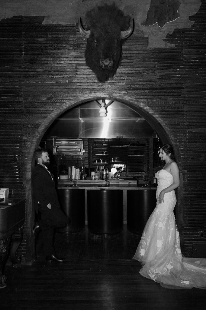 A couple leans on an brick wall in elopement attire at the saloon in The Western Hotel.