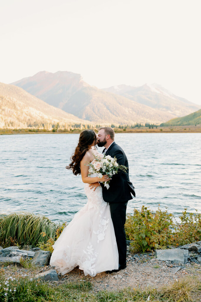A bride holds a bridal bouquet while kissing her husband in Ouray.