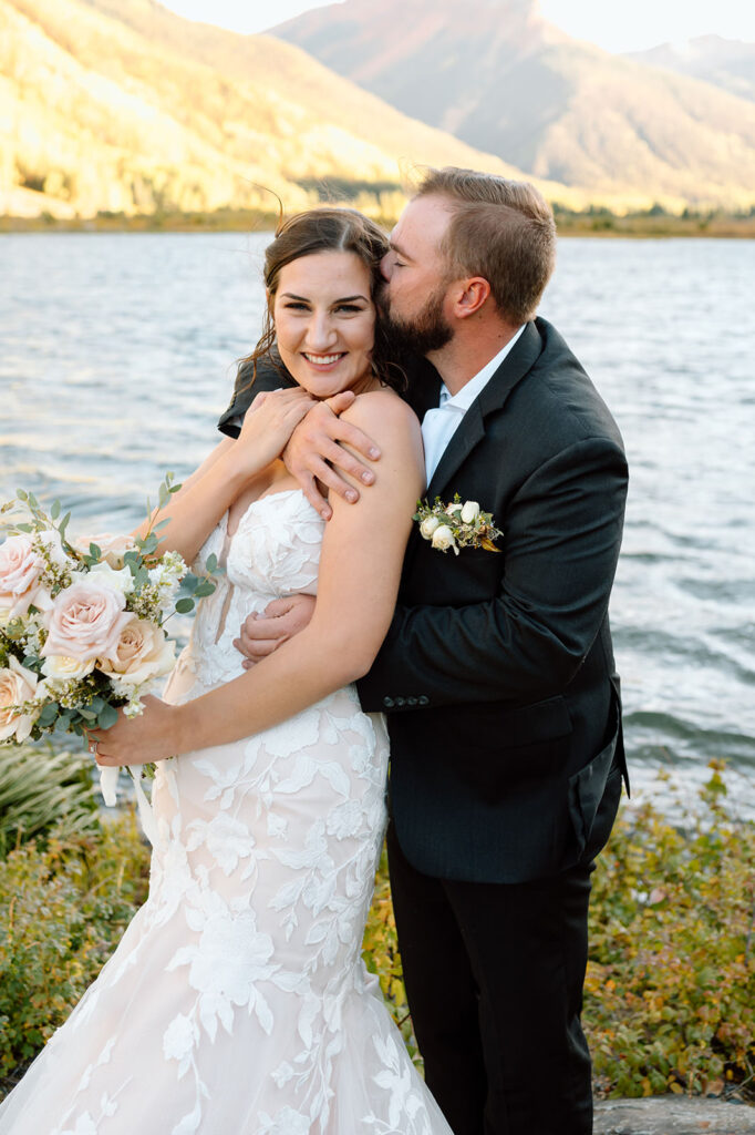 A groom kisses his bride while lakeside celebrating their adventure elopement. 