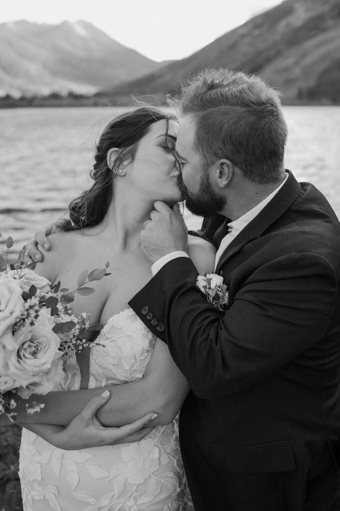 A newly married couple kisses near a alpine lake in Colorado. 