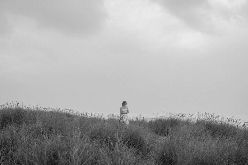 A bride stands in a seagrass meadow at Cannon Beach.
