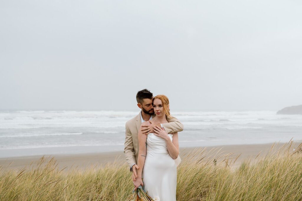 A bride and groom embrace near the Pacific Ocean.