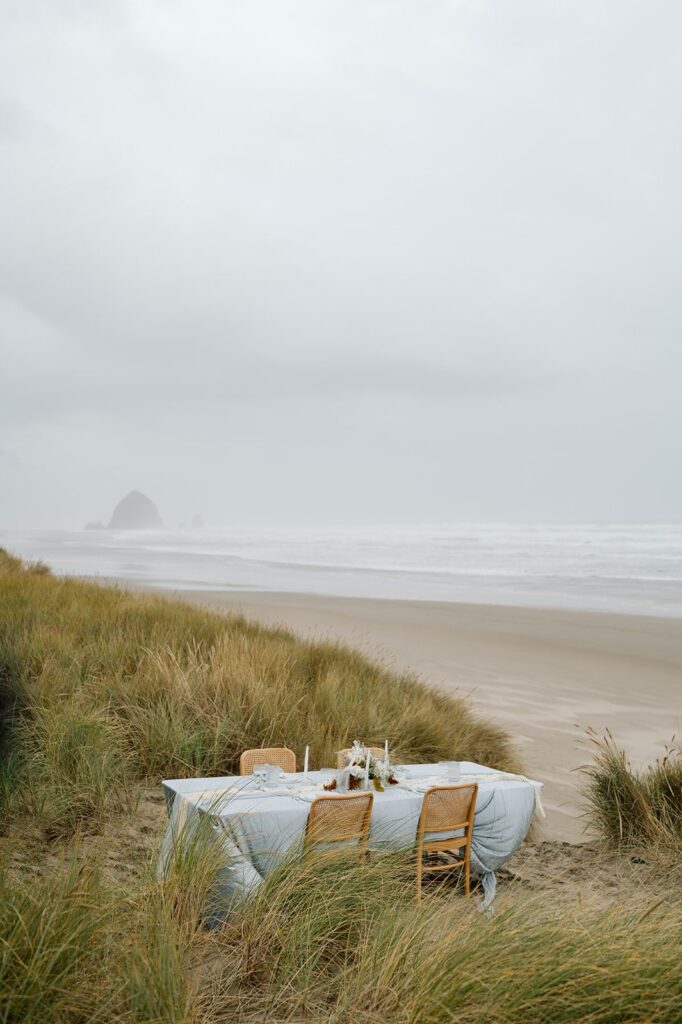 A reception table with a blue tablecloth is set up on Cannon Beach. 