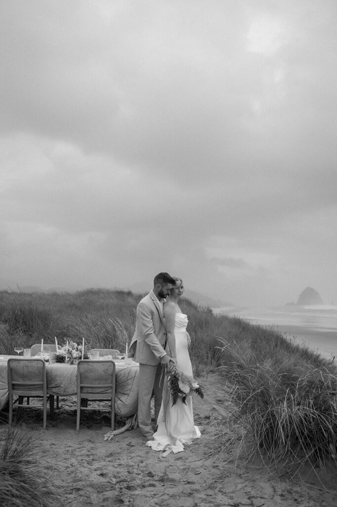 A couple embraces near their sweetheart table at their beach wedding reception. 