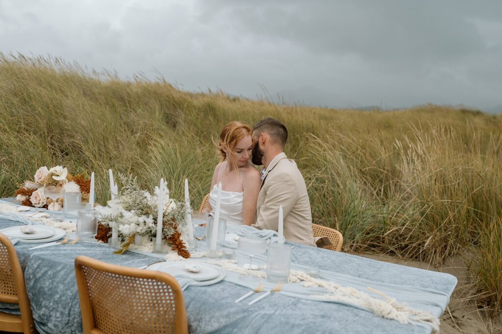 A couple sits at a coastal tablscape in celebration of their wedding in Oregon. 