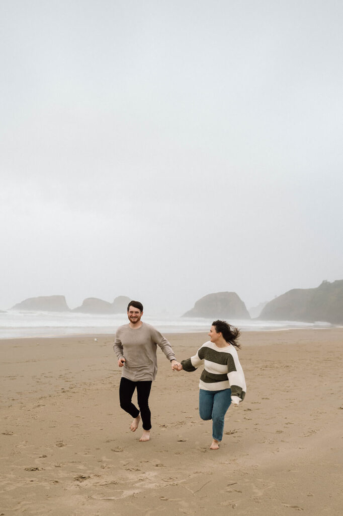 A couple holds hands while running on a beach in Oregon. 