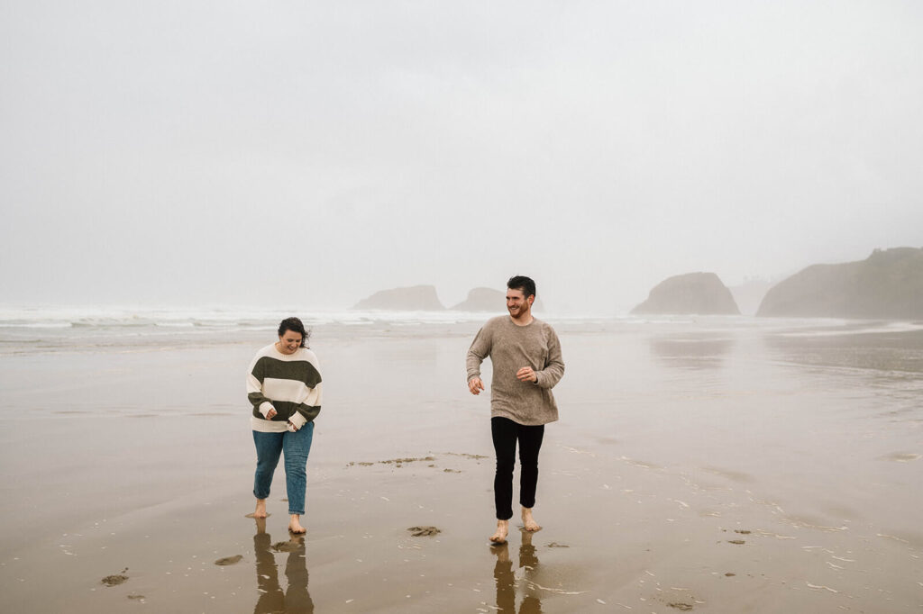 A couple walks along Cannon Beach during their romantic engagement session. 