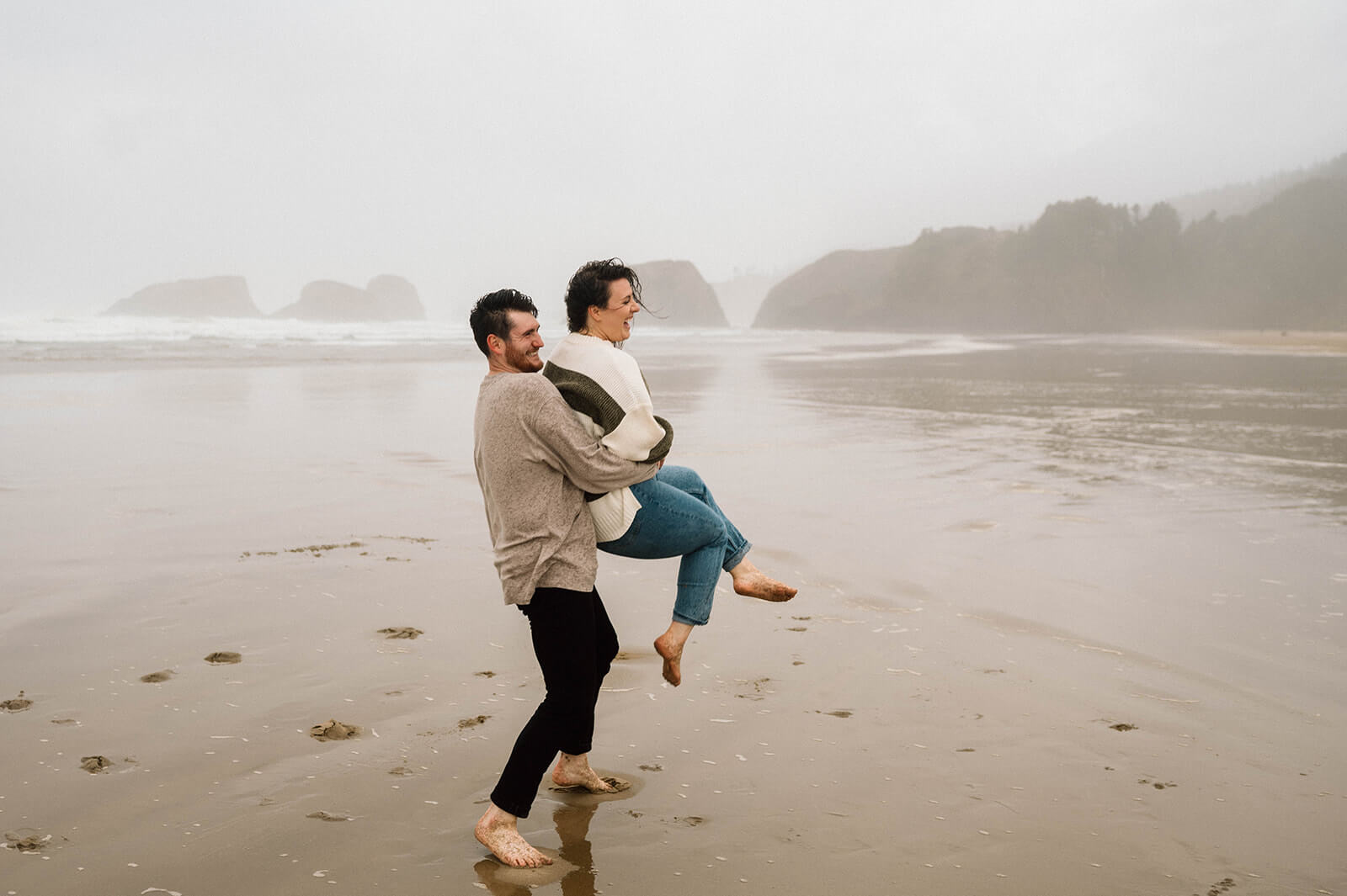 A man lifts a woman out of the sand and twirls her on Cannon Beach.