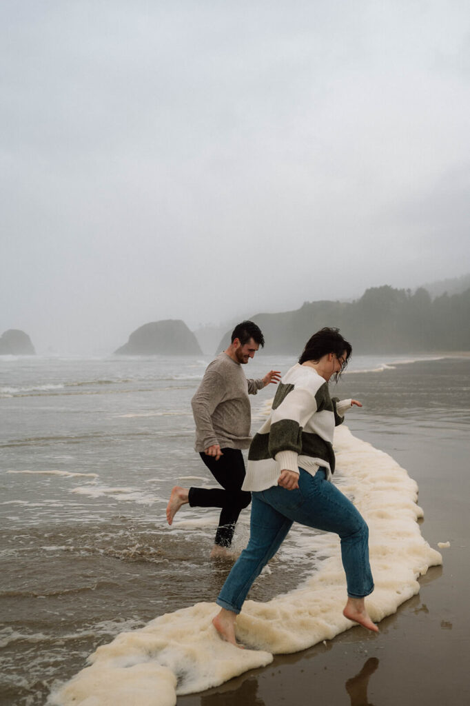 A couple runs out of the surf during their beach engagement session.