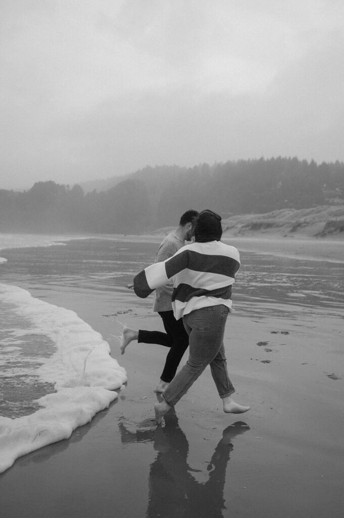 A couple holds hands and runs out of the surf on Cannon Beach. 