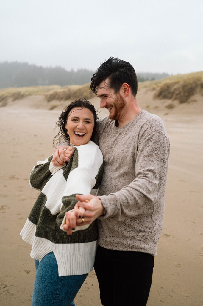 A couple smiles at one another while it's raining on an Oregon beach.