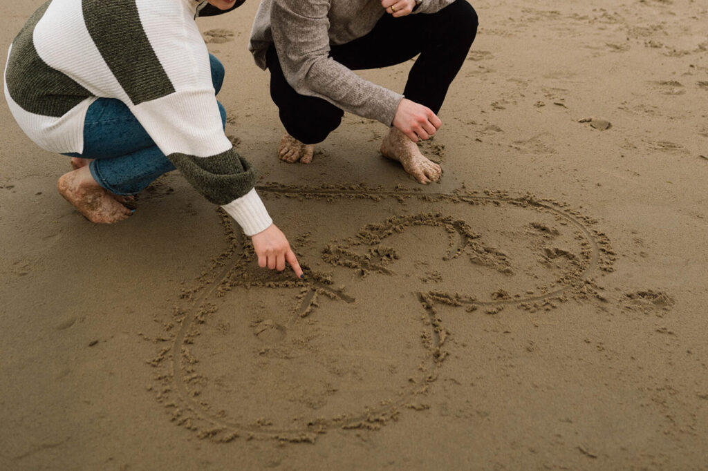 A couple draws a heart in the sand with their initials on Cannon Beach. 