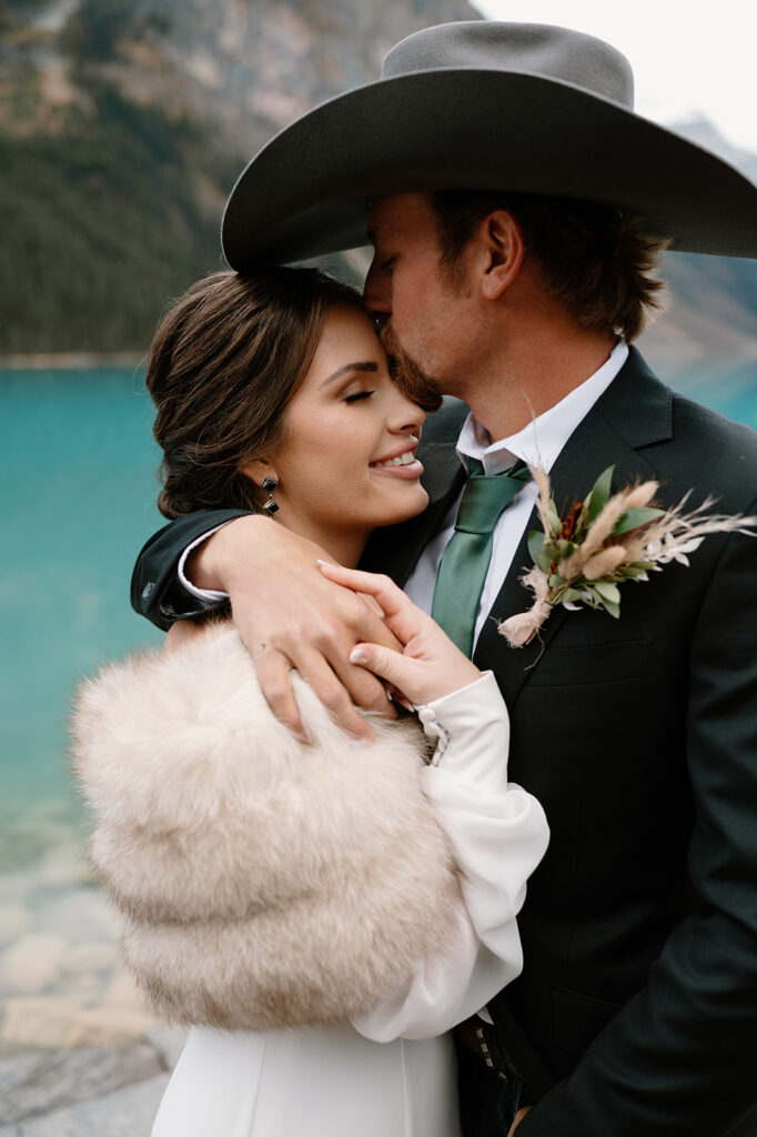 A man kisses his bride's forehead after celebrating their Lake Louise vow ceremony in Banff.